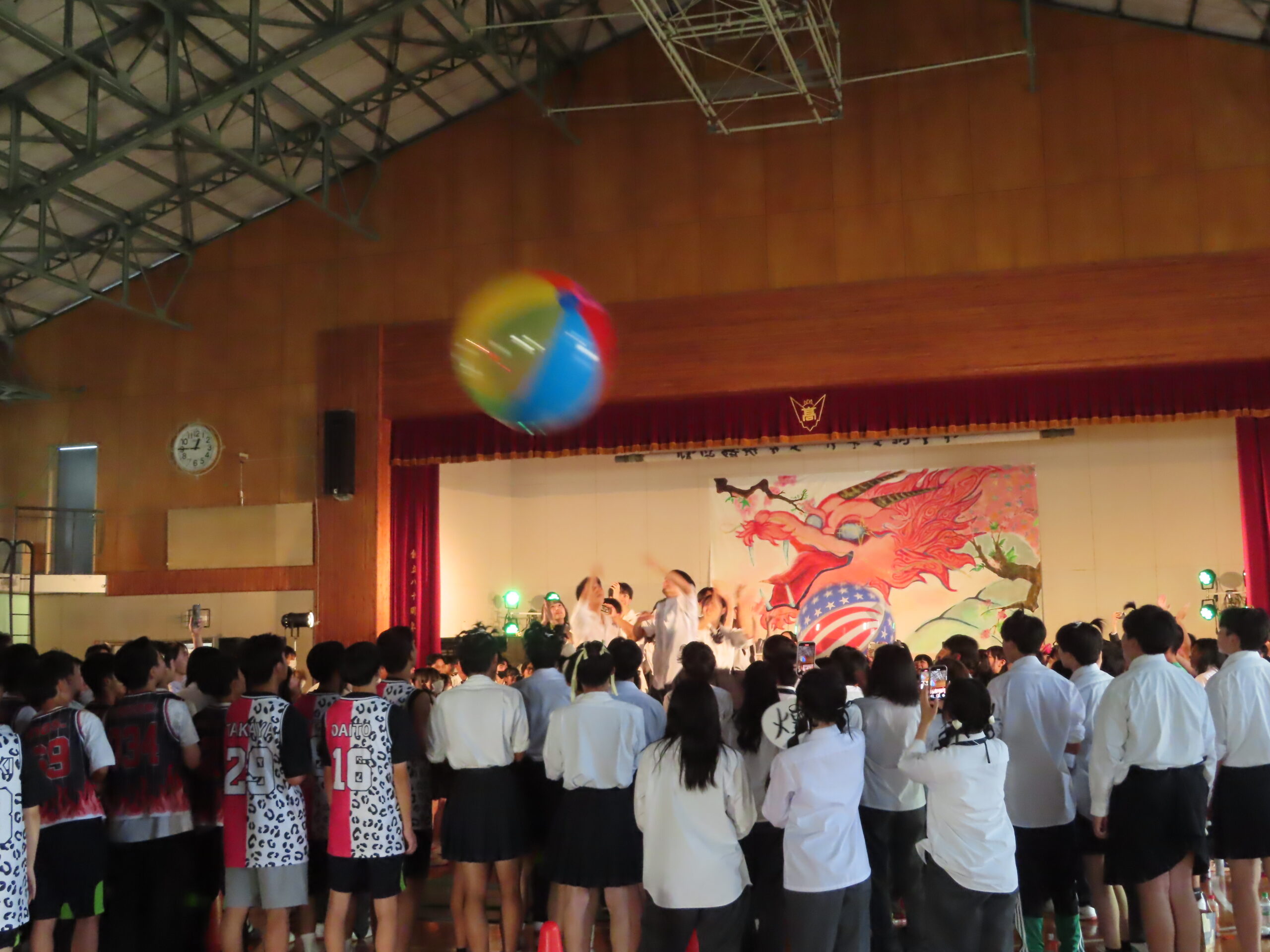 文化祭のステージイベントで、大きなビーチボールを飛ばして盛り上がる生徒たち